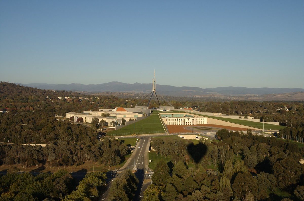 Parliament House in Canberra seen from the air at dusk, framed by bushland and hills
