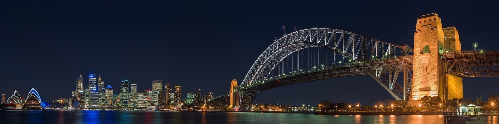 The Sydney Harbour Bridge lit at night, with the city skyline and Opera House behind it
